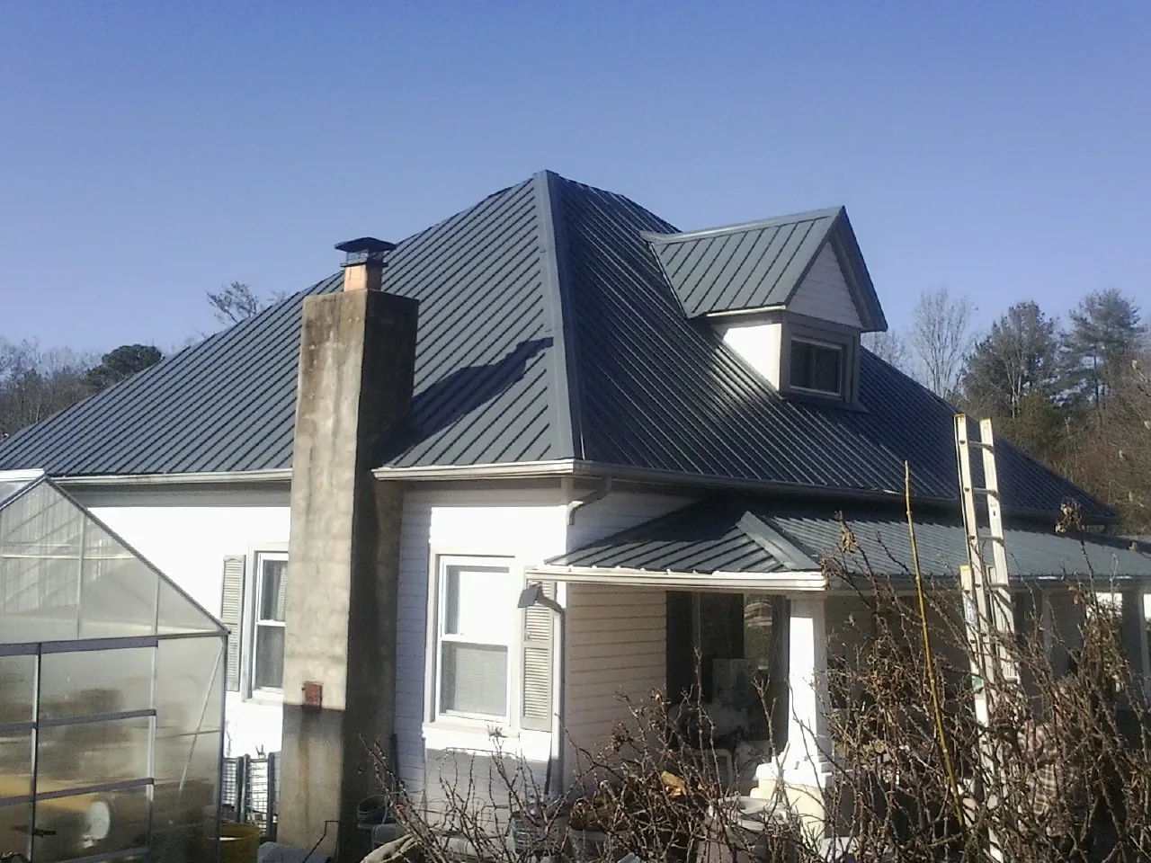 Dark blue standing seam metal roof on a white farmhouse with dormer — Slate & Tile Roof Repair by Roofing Brothers in Maspeth