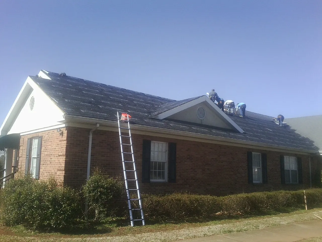 Crew tearing shingles off a brick ranch roof with a ladder set — Emergency Roof Repair work by our crew in Maspeth