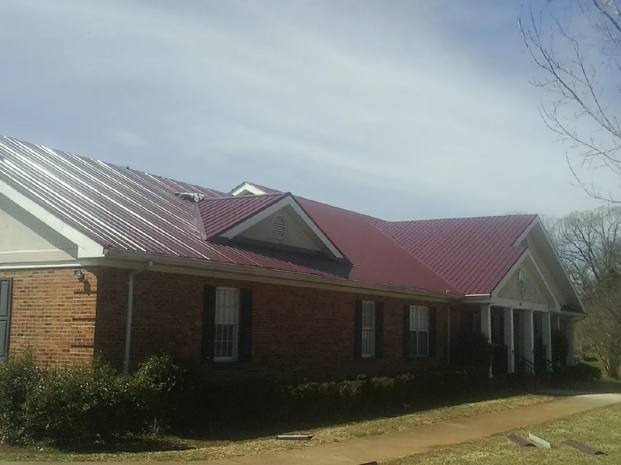 Red metal roof with gabled entries on a long brick building, from a Hail Damage Roof Repair job in Maspeth