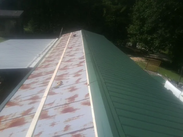 Old rusted panels beside newly installed green metal roofing — Wind Damage Roof Repair by Roofing Brothers in Maspeth