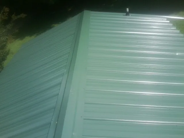 New green metal panels meeting at the ridge of a roof — Flat Roof Repair work by our crew in Maspeth