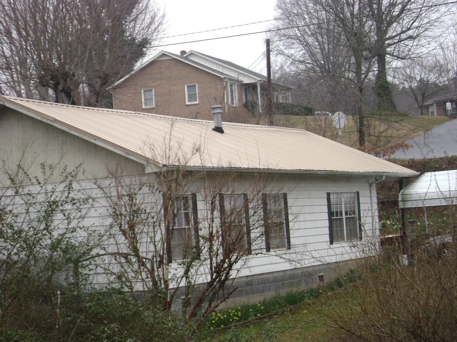 Tan metal roof on a white sided house set into a hillside — Commercial Roofing by Roofing Brothers in Maspeth