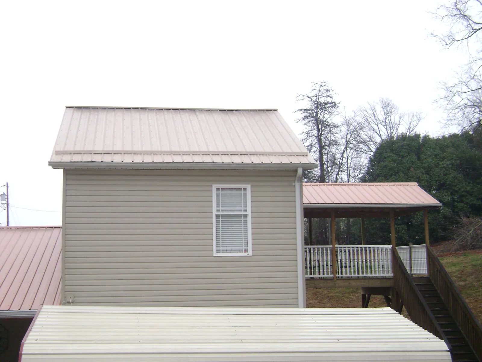 Tan metal roofs on a two story addition and attached porch, from a Roof Replacement job in Maspeth